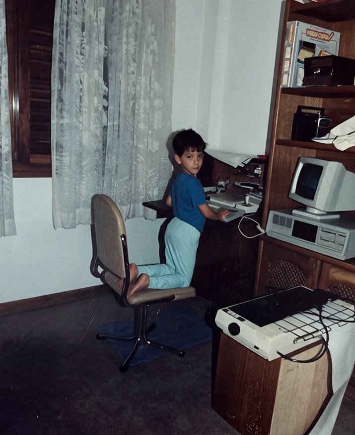 Felipe aos quatro anos, ajoelhado em uma cadeira, usando o computador no quarto, em 1990